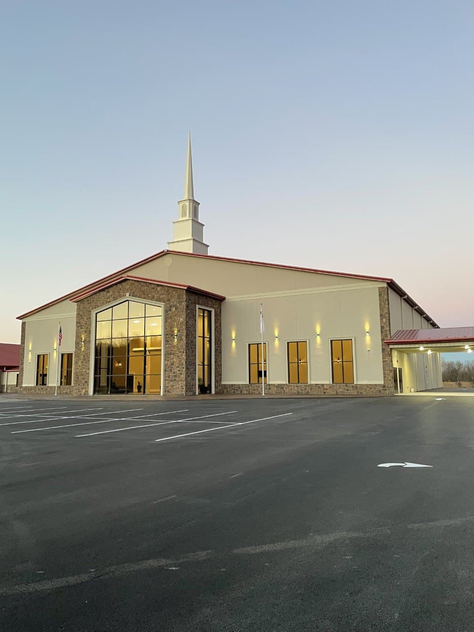 The Maple Springs church building at dusk, its tall windows glowing gold under a pink and blue Arkansas sky