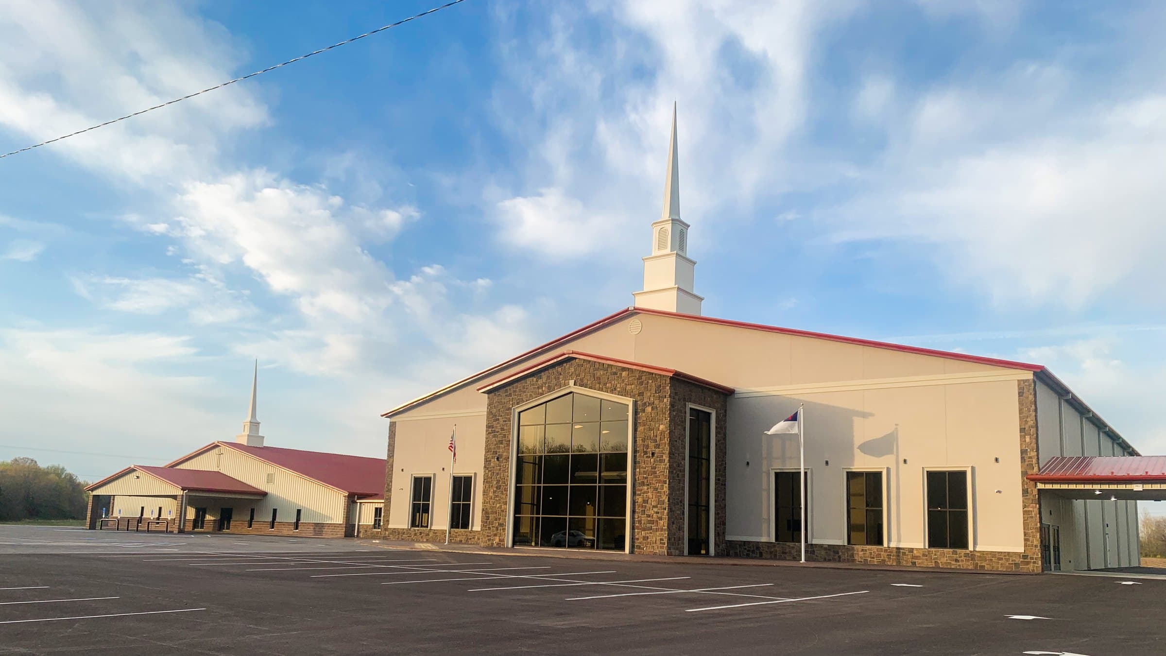 The Maple Springs Missionary Baptist Church building in Rosie, Arkansas — cream walls, fieldstone entry, a red metal roof, and a white steeple against a blue Arkansas sky